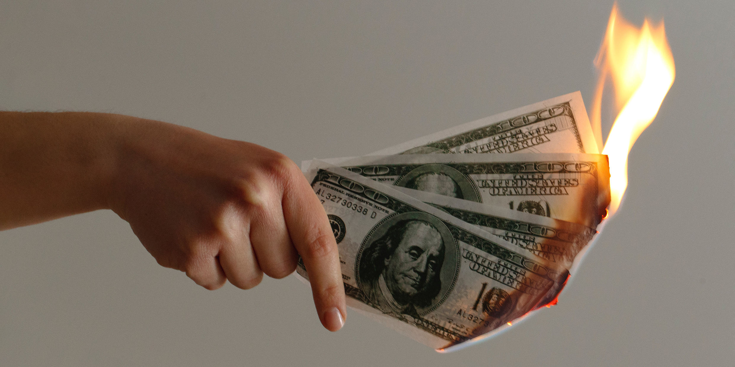 Image of hand holding burning 100 dollar bills