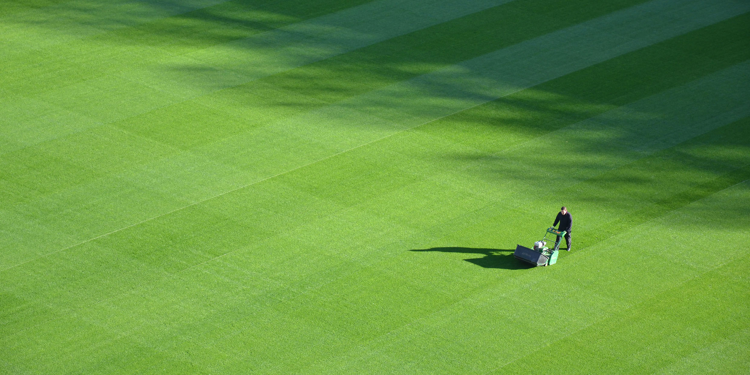 Image of man pushing lawnmower across wide expanse of grass