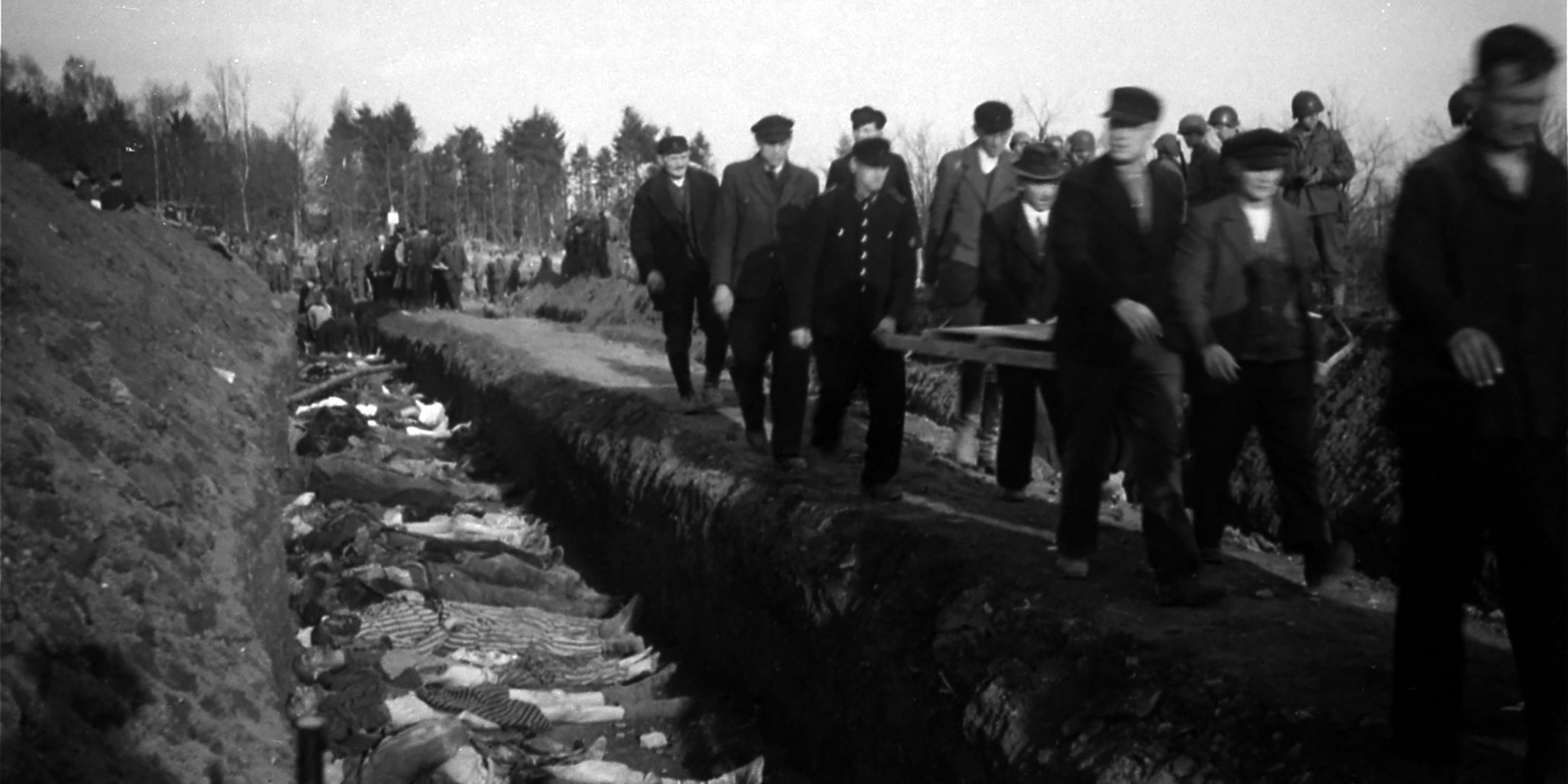 Image of German civilians walking past open mass grave filled with corpses
