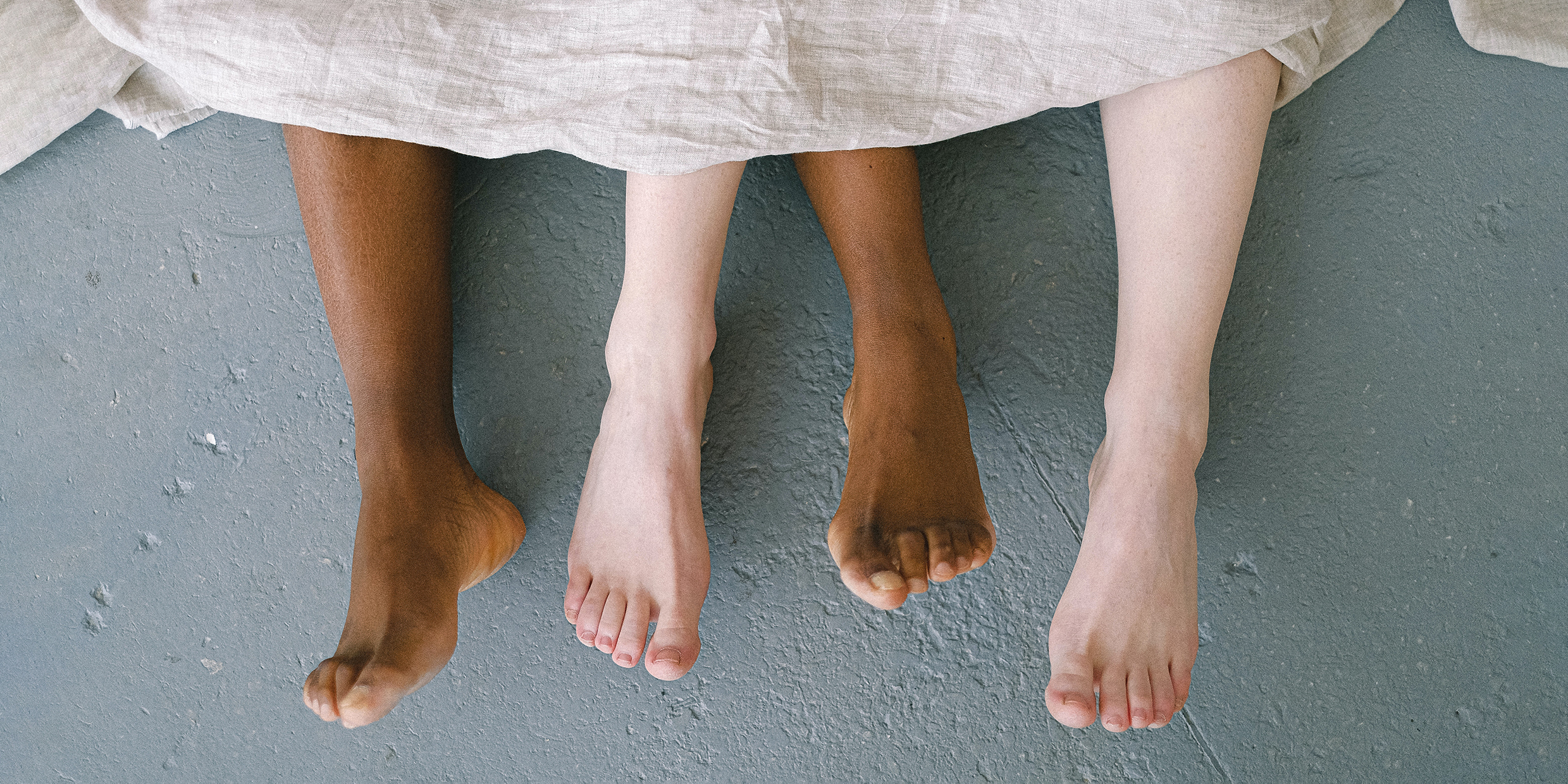 Image of two pairs of bare feet emerging from under bed sheet