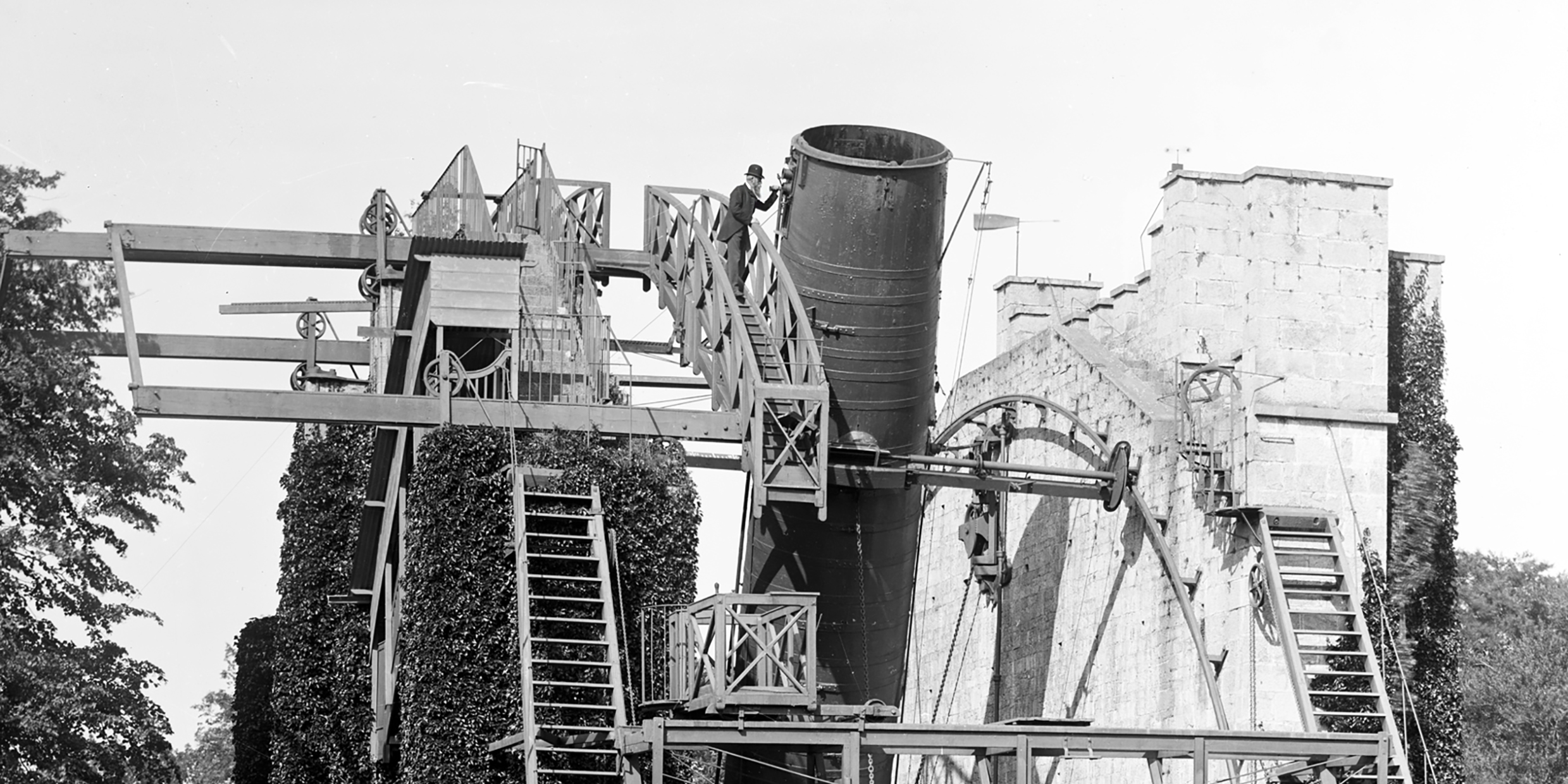 Black-and-white image of man dwarfed by enormous telescope