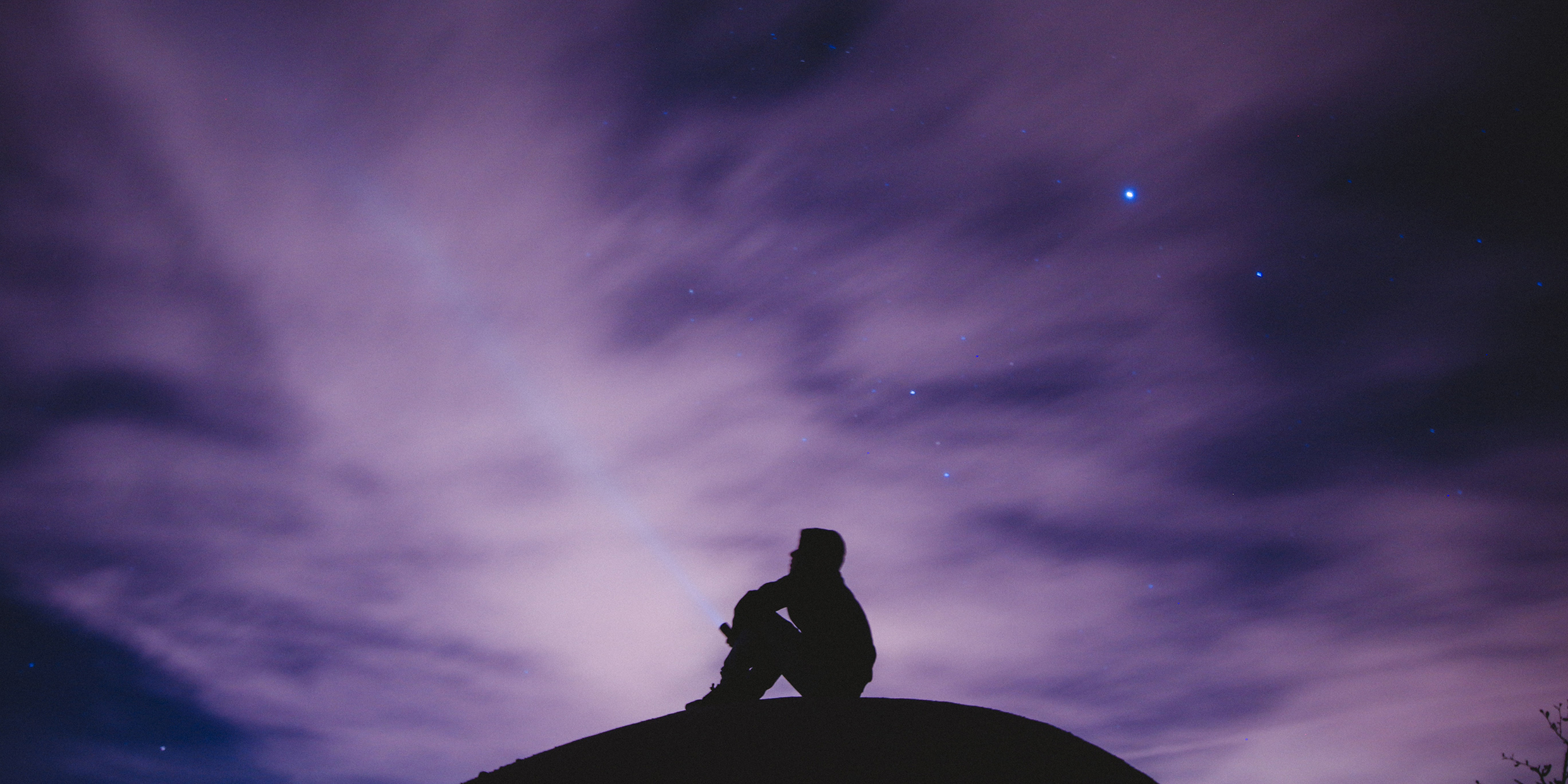 Image of silhouetted man sitting under the night sky