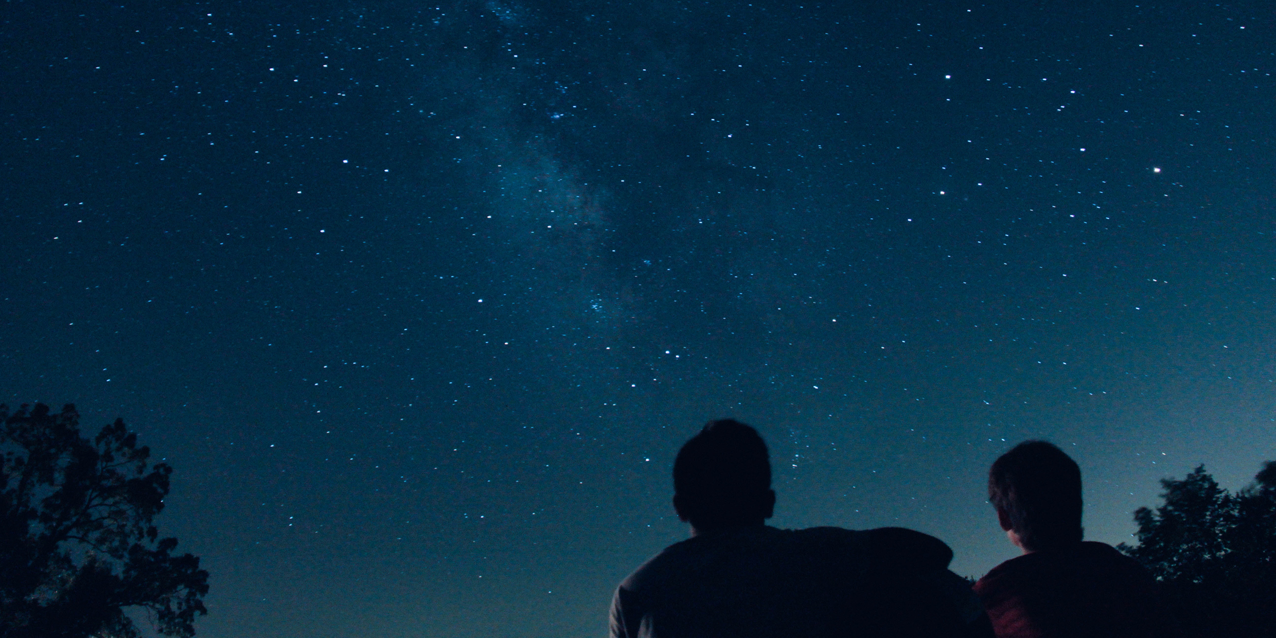 Image of two silhouetted figures underneath the night sky