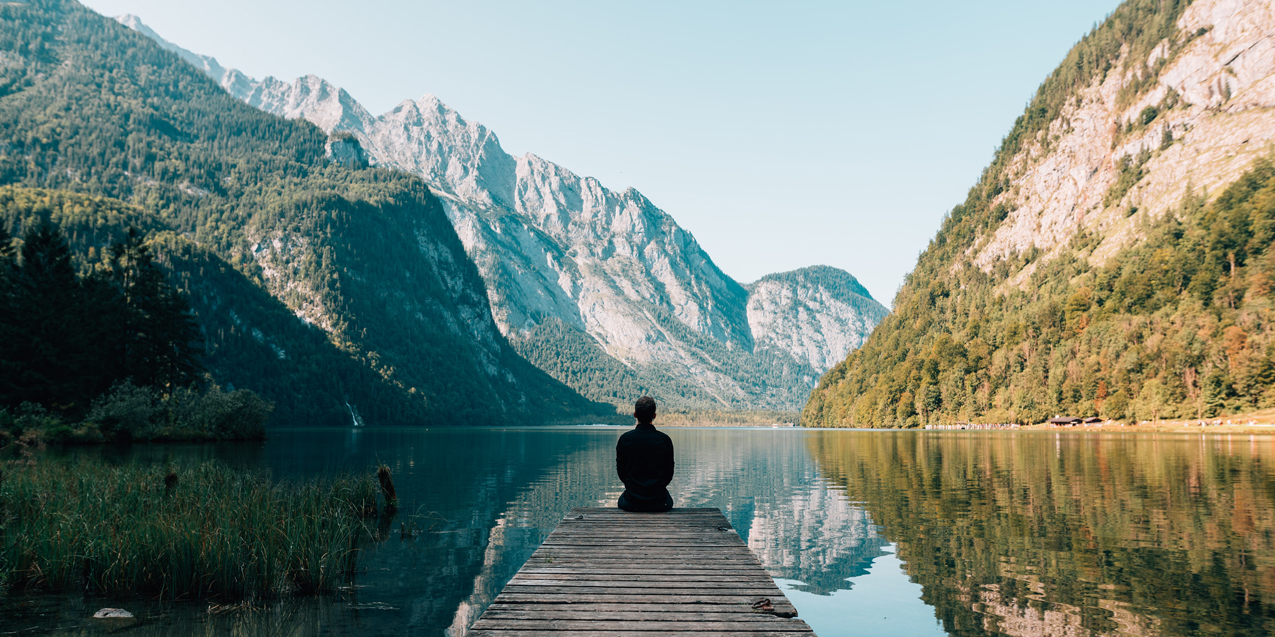 Image of man seated on dock looking a beautiful mountain lake