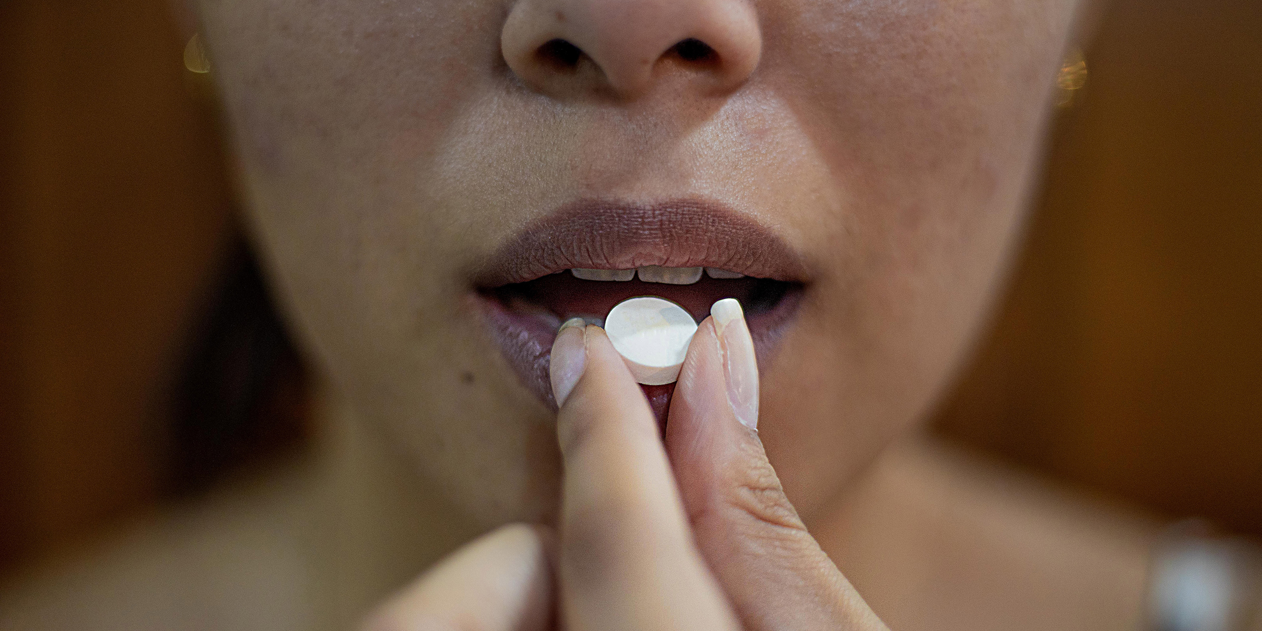 Close up image of a woman placing a pill into her mouth
