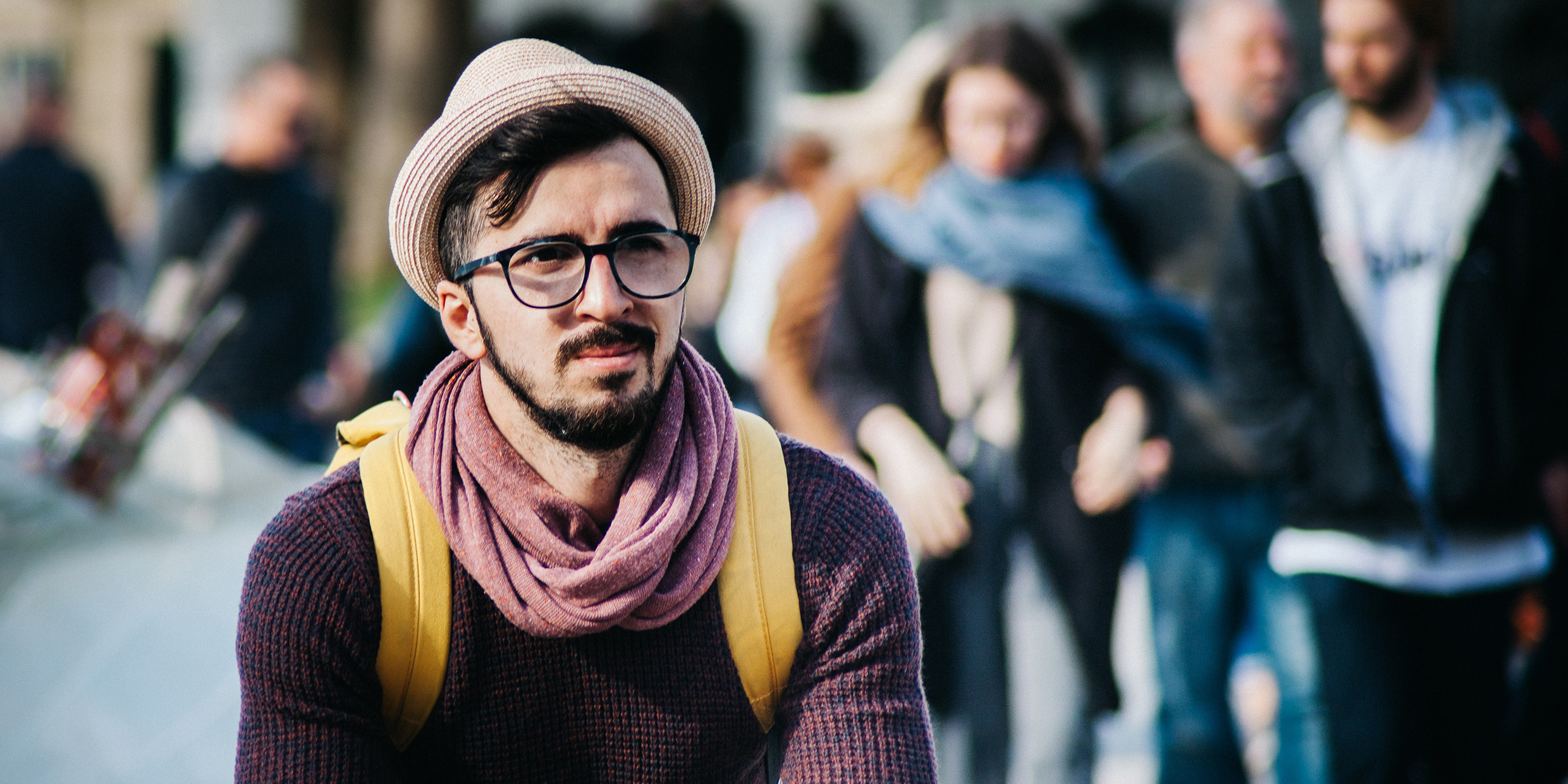 A man with stylish hat, scarf, and glasses looking thoughtful
