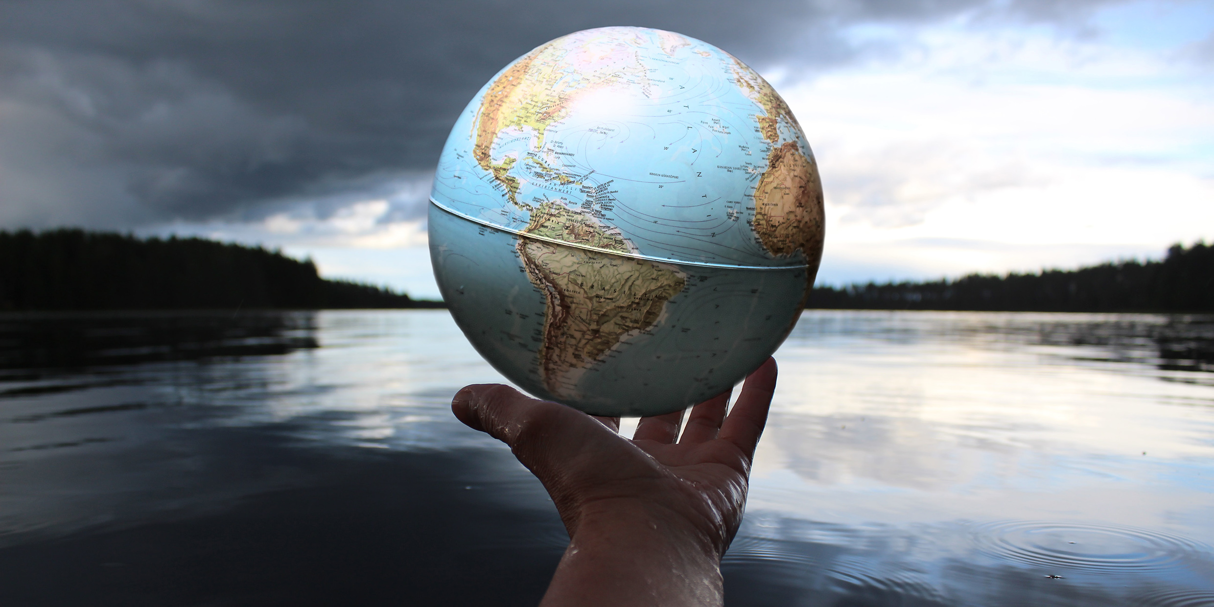 Image of hand holding a small globe in front of a natural environment