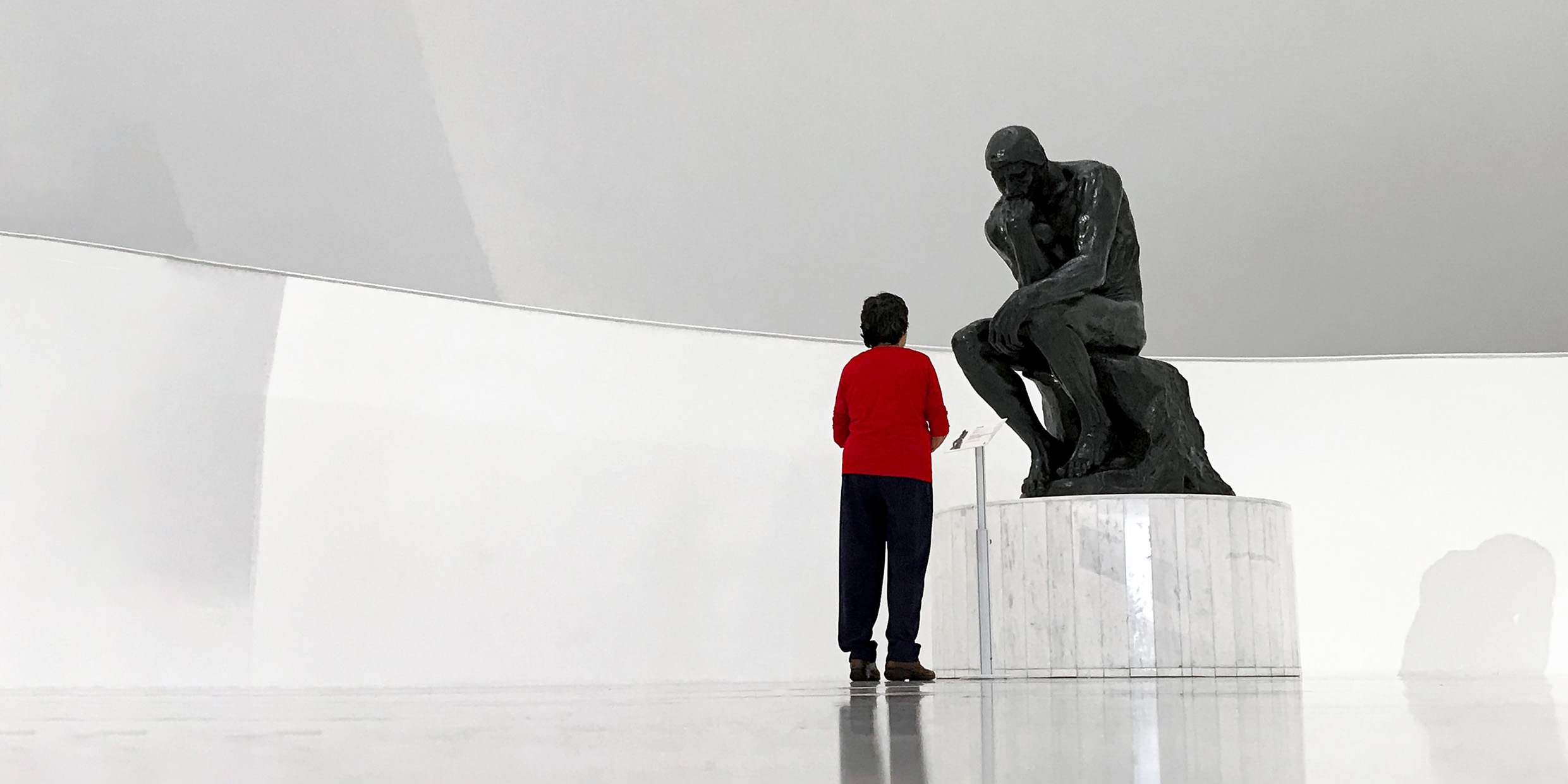 Image of person standing next to the famous sculpture of "The Thinker" inside a museum