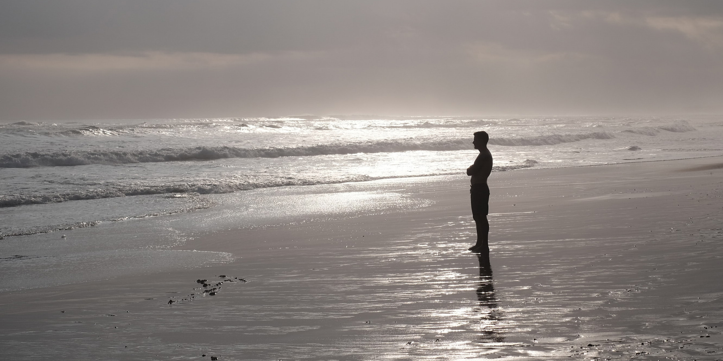 Image of man standing on beach looking out at the ocean