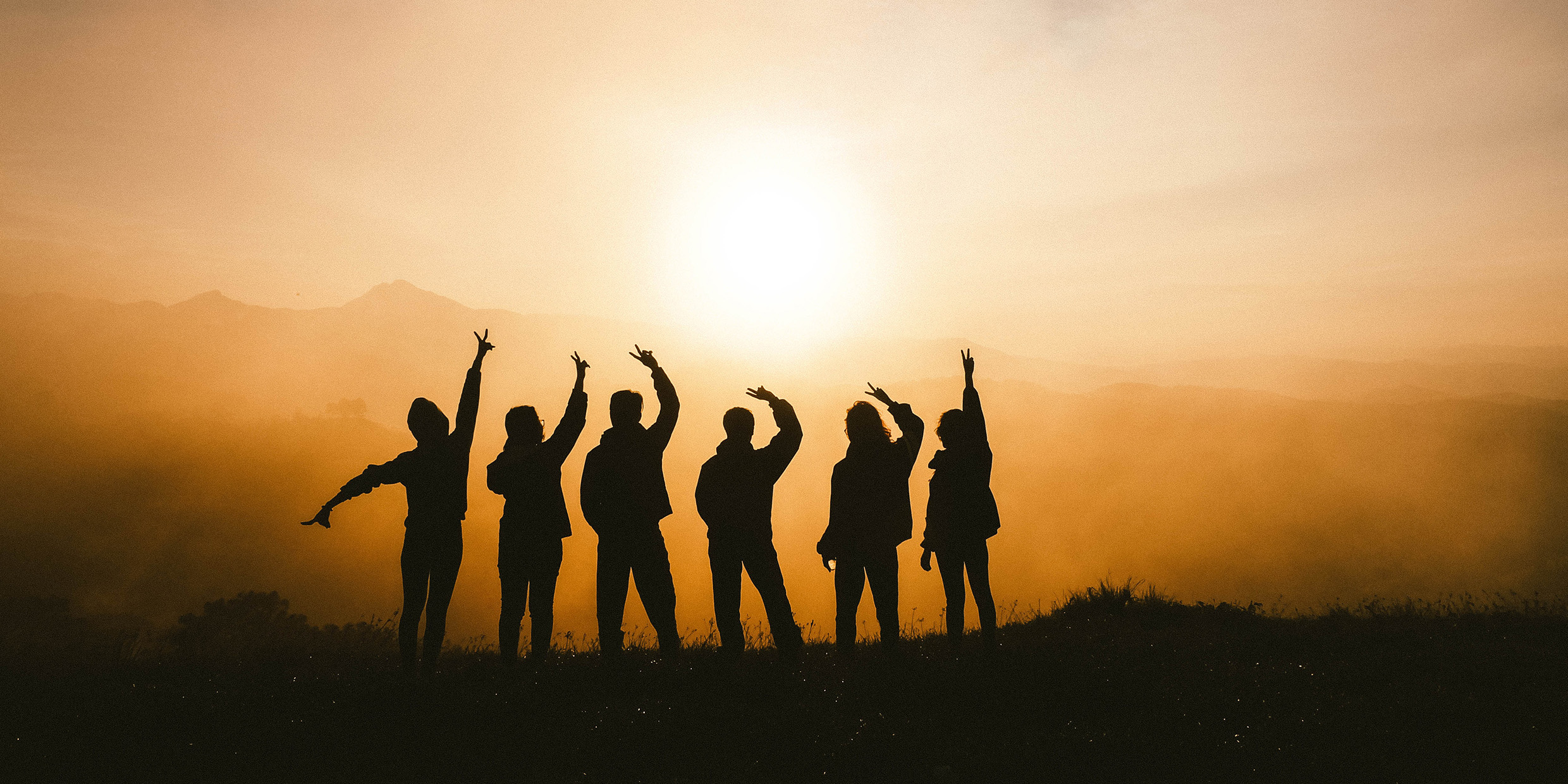 Image of a group of people silhouetted by a setting sun